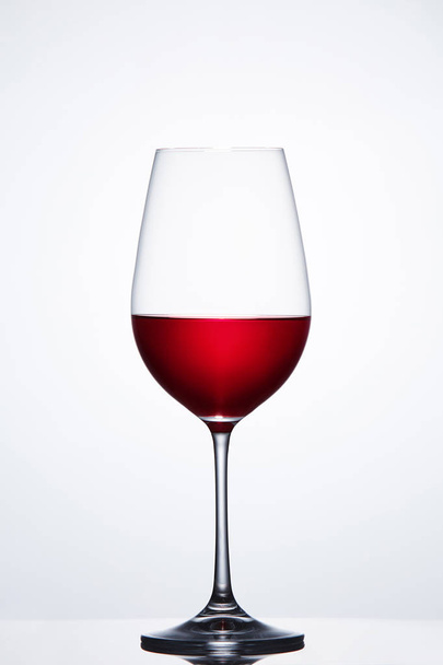 Red wine in the fragile pure wineglass standing against light bckground with reflection. - Foto, afbeelding