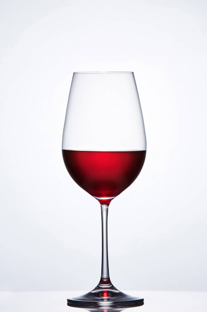 Elegant crystal wine glass with red wine against light background with reflection. - Zdjęcie, obraz