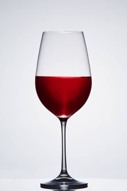 Fragile elegant wineglass of red wine standing against light background. - Fotoğraf, Görsel