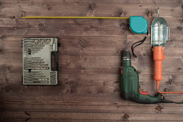 Электрическая дрель, рулетка, крученые детали и лампа на деревянной
  - Фото, изображение