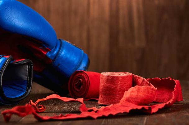 Close-up of the blue boxing gloves and red bandage on wooden background. - 写真・画像