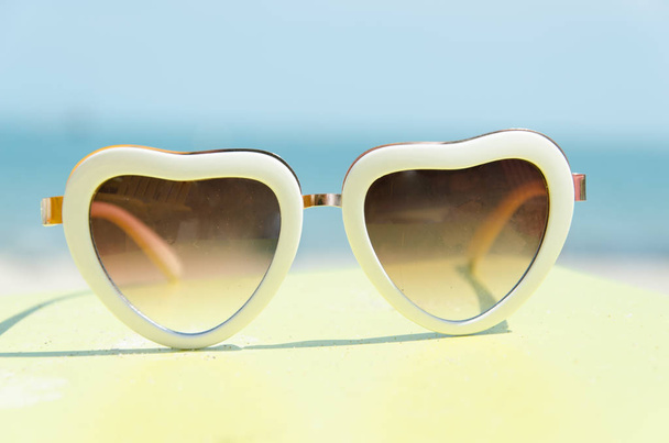 Módní sluneční brýle srdce ve tvaru žluté stojanu s pozadím modré moře - Fotografie, Obrázek