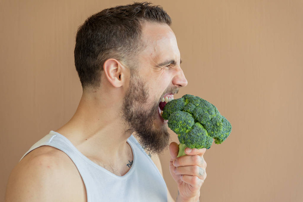 A guy with a beard sniffs broccoli - Foto, afbeelding