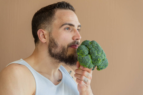 A guy with a beard sniffs broccoli - Фото, изображение