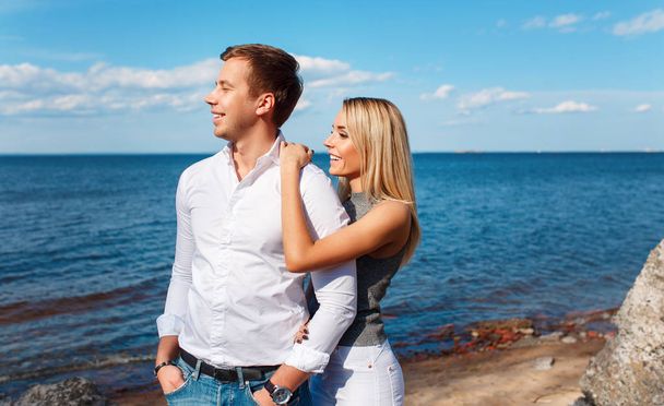Happy couple on sea background. Happy young couple laughing and hugging on the beach - 写真・画像