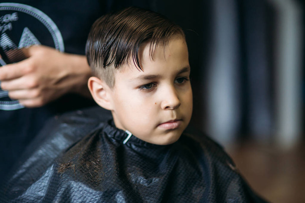 小さな男の子が理髪店の椅子に座りながら床屋で散髪を取得. - 写真・画像