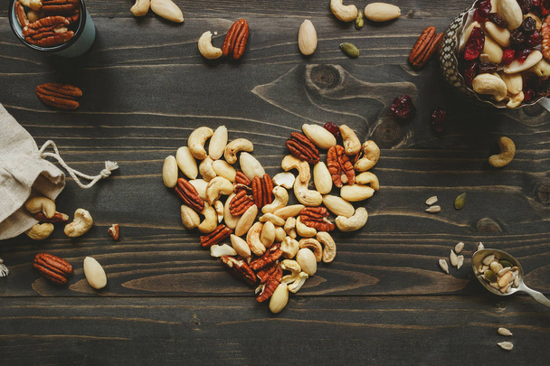 Las nueces se mezclan en forma de corazón en la mesa de madera. Las nueces se mezclan con semillas y frutos secos en la mesa de madera
 - Foto, imagen