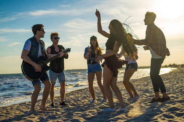Mutlu arkadaş sahilde dans. Adam gitar oynuyor - Fotoğraf, Görsel