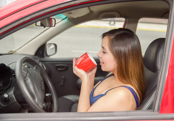 Beautiful young woman drinking a cup of coffe or tea, while the car drives by itself - 写真・画像