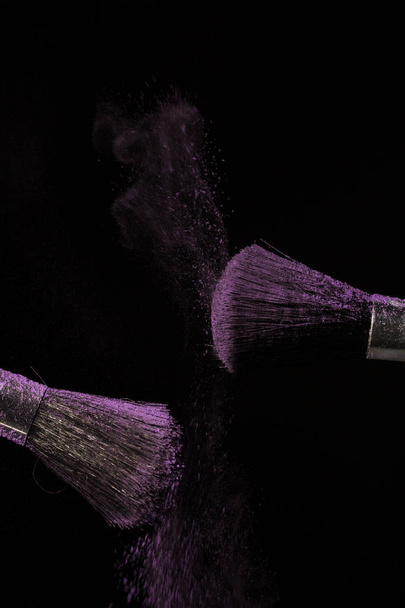 Maquillaje cepillo con polvo púrpura sobre fondo negro
 - Foto, Imagen