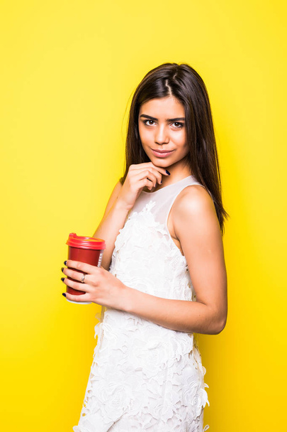 黄色の背景でコーヒーを飲む若い都市カジュアルな女性 - 写真・画像