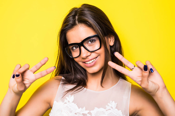 Mladá dívka, která nosí brýle s gestem vítězství v žlutém pozadí. Dívka na kameru. - Fotografie, Obrázek