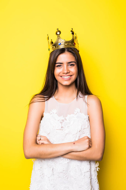 Beautiful young woman wearing crown and nice dress on yellow background - Photo, Image