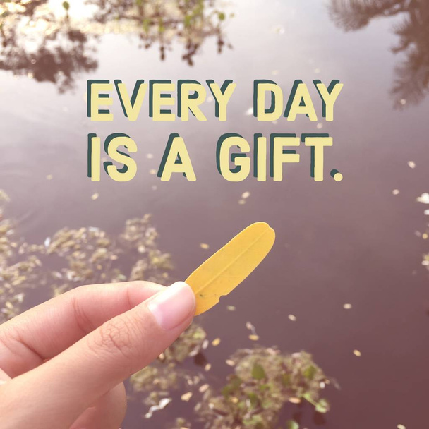Citation "chaque jour est un cadeau" sur la main de la femme tenant une feuille jaune
  - Photo, image