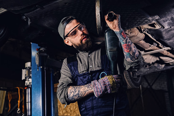 Bearded mechanic holds angle grinder - Фото, изображение