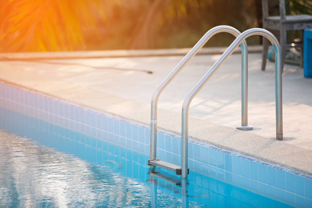 Grab bars ladder in the blue swimming pool with Orange sun light - Photo, Image