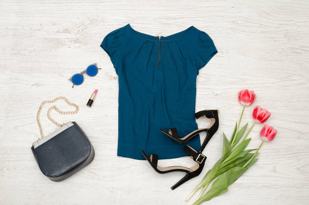 Fashion concept. Blue blouse, handbag, round glasses, lipstick, black shoes and pink tulips. Top view, light wood background - Photo, Image