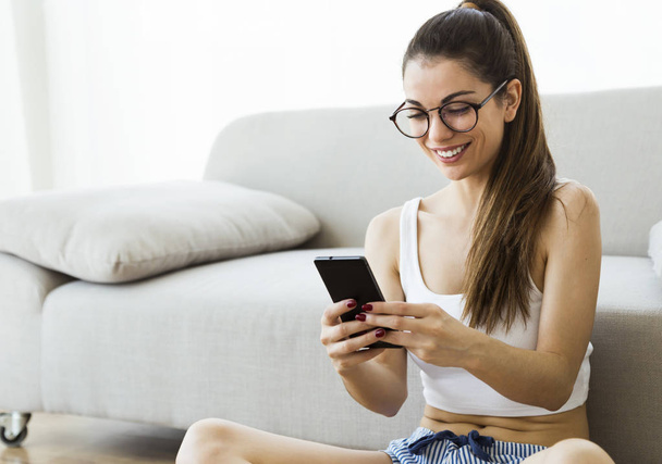 Beautiful young woman using her mobile phone at home. - Foto, imagen