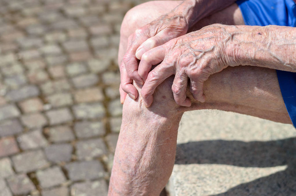 alter Mann mit knorrigen Händen, die sein Knie umklammern - Foto, Bild