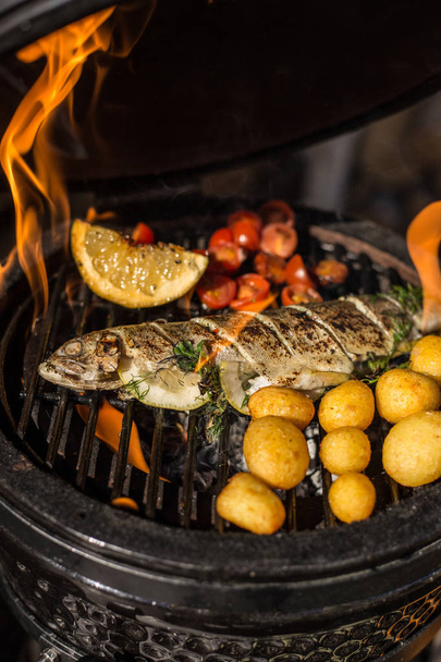Delicious rainbow trout fish with tomatoes, potatoes and lemon cooking on hot flaming grill. Barbecue. Restaurant - Foto, Imagen