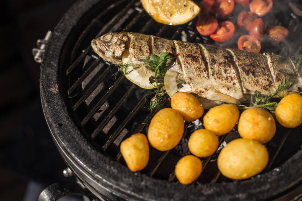 Delicious rainbow trout fish with tomatoes, potatoes and lemon cooking on hot flaming grill. Barbecue. Restaurant - Foto, immagini