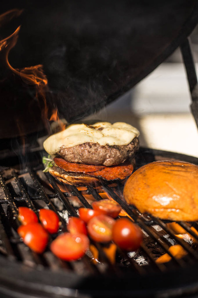 Delicious cheeseburger with tomatoes cooking on hot flaming grill. Barbecue. Restaurant - Foto, immagini