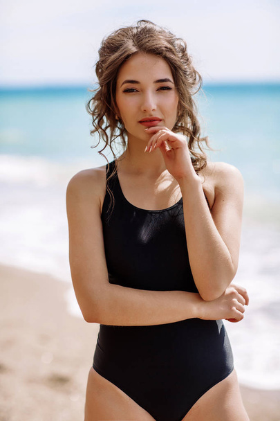 High fashion look.glamor beautiful sexy stylish brunette young female model with bright make-up, with perfect sunbathing clean skin in a black swimsuit on the beach in fashion style - 写真・画像
