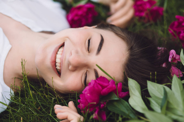 Woman lying on grass with flowers peonies around - Fotoğraf, Görsel