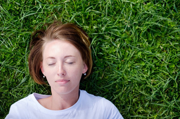 Une belle fille avec des taches de rousseur repose sur l'herbe verte
 - Photo, image