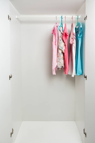 Kleider hängen in weißer Garderobe am Geländer.  - Foto, Bild