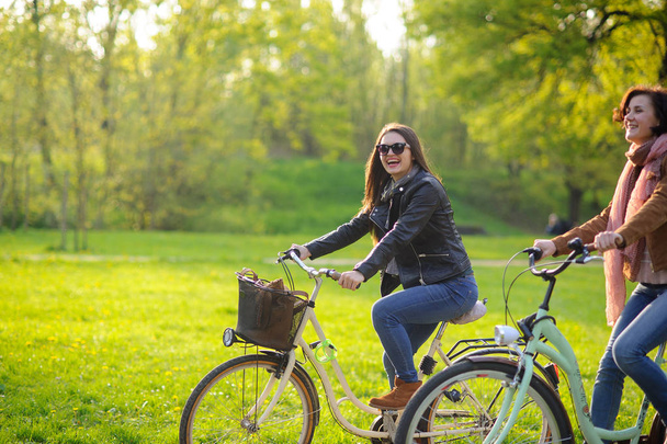 Two young women ride bikes in the spring park. - 写真・画像