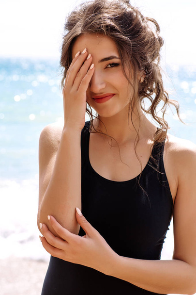 high fashion look.glamour schöne sexy stilvolle brünette junge weibliche Modell mit hellem Make-up, mit perfektem Sonnenbaden saubere Haut in einem schwarzen Badeanzug am Strand in Mode-Stil - Foto, Bild
