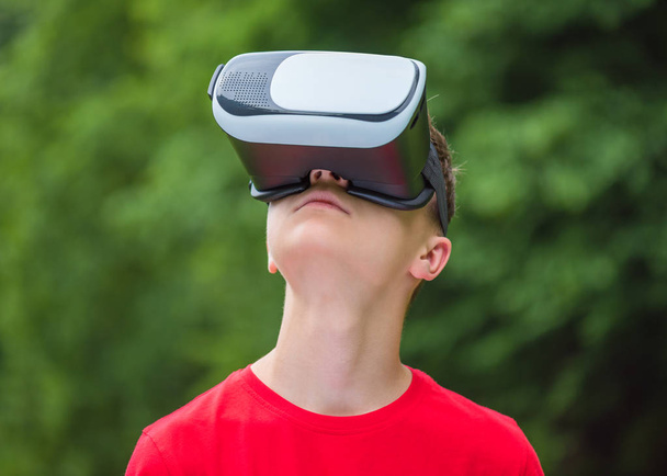 Teen boy with VR glasses in park - Фото, изображение