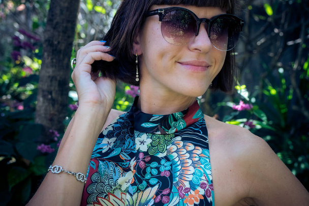 Привлекательная молодая женщина в красивом шелковом платье среди тропических растений. Отпуск. Тропики. Модный снимок. Бали
. - Фото, изображение
