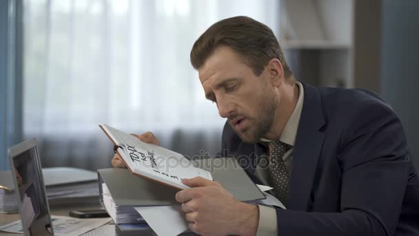 Tired company employee looking at to do list in notebook drained out of strength - Кадри, відео