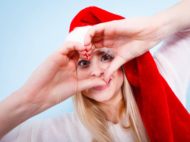 Girl in santa claus hat making heart symbol with fingers - Foto, afbeelding