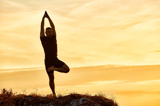 Silhouette of the man practicing yoga on the hill against beautiful sunset. - Photo, Image