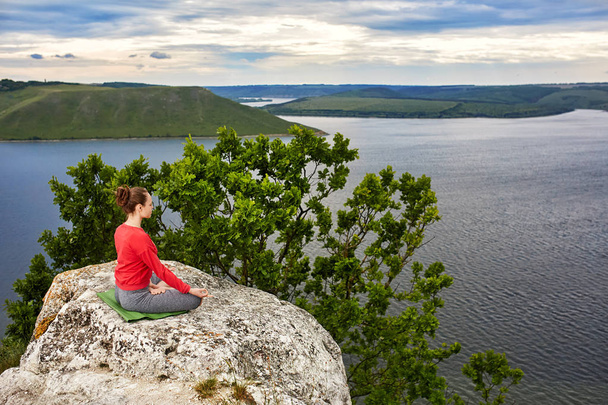 Giovane donna che medita in una posa di loto sulla roccia sopra il grande fiume
. - Foto, immagini