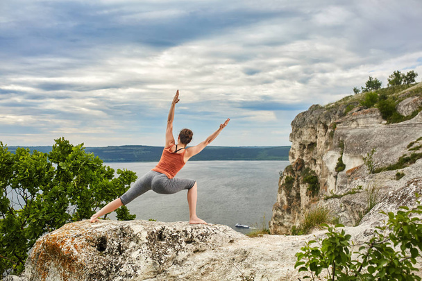 An attractive young woman doing a yoga pose for balance on the rock. - Fotoğraf, Görsel