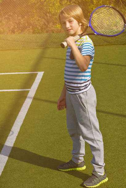 Junge steht mit Tennisschläger und Ball auf dem Platz - Foto, Bild