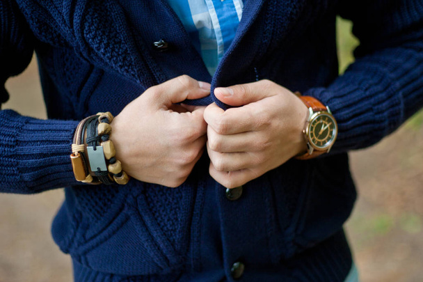 Модный портрет молодого бизнесмена красивого образцового мужчину в повседневном костюме с аксессуарами на руках, стальными часами, серыми джинсами и браслетами
 - Фото, изображение