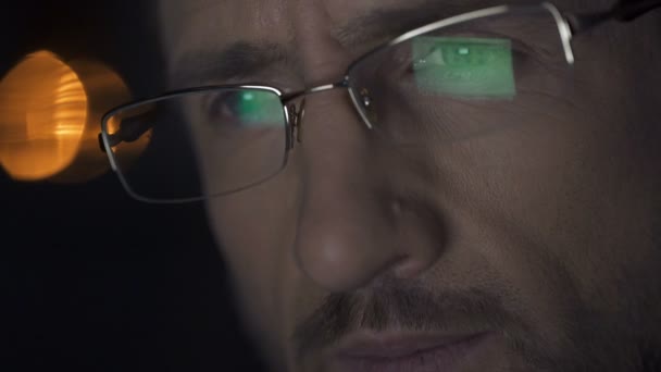 Man working on laptop at night, laptop screen with files reflected in glasses - Záběry, video