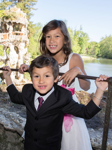 δύο παιδιά αδελφός και αδελφή στην άκρη μιας λίμνης είναι ντυμένα για τα γενέθλια ή την τελετή - Φωτογραφία, εικόνα