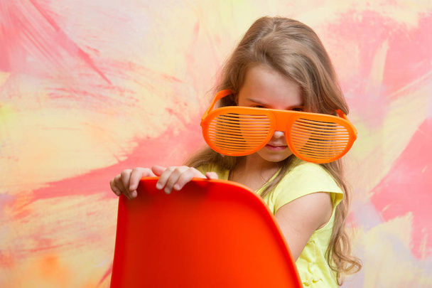 kid sitting on orange chair in summer glasses - Photo, Image