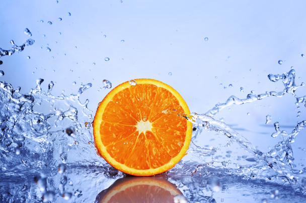 Juicy half an orange in splash of blue water - Fotó, kép