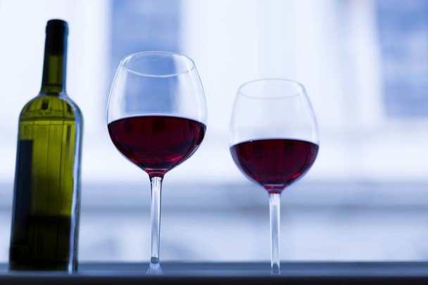 2 ποτήρια και ένα μπουκάλι κόκκινο κρασί που κάθεται σε ένα ανοιχτό παράθυρο σε μια ευρωπαϊκή πόλη. - Φωτογραφία, εικόνα