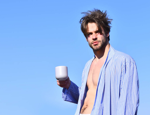 Caucasian macho in blue striped pajamas holding cup - Fotó, kép