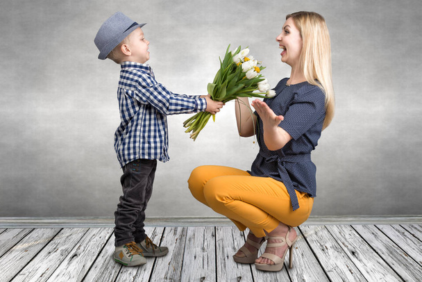 Small son gives his beloved mother a bouquet of beautiful tulips. Spring, concept of family vacation. Women's day. - Photo, image