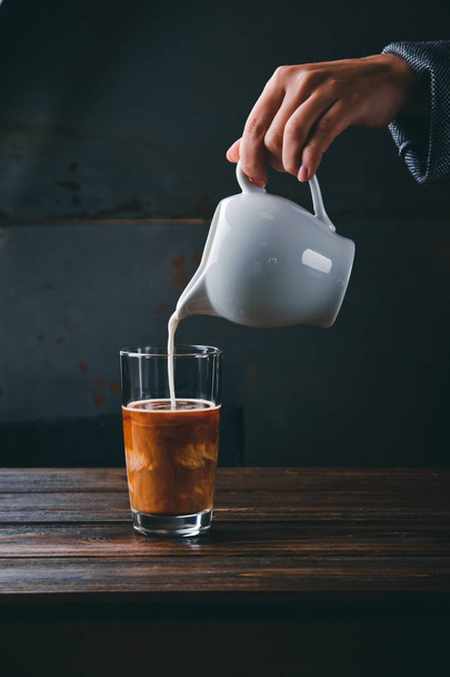 Nahaufnahme von Barista-Mädchenhänden bei der Zubereitung des richtigen Cappuccino, der Milch in ein Glas Kaffee gießt. Konzept des leckeren Aroma-Kaffees - Foto, Bild