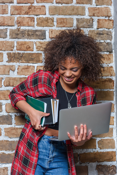 young stylish woman smiling while holding laptop and notebooks - Photo, Image